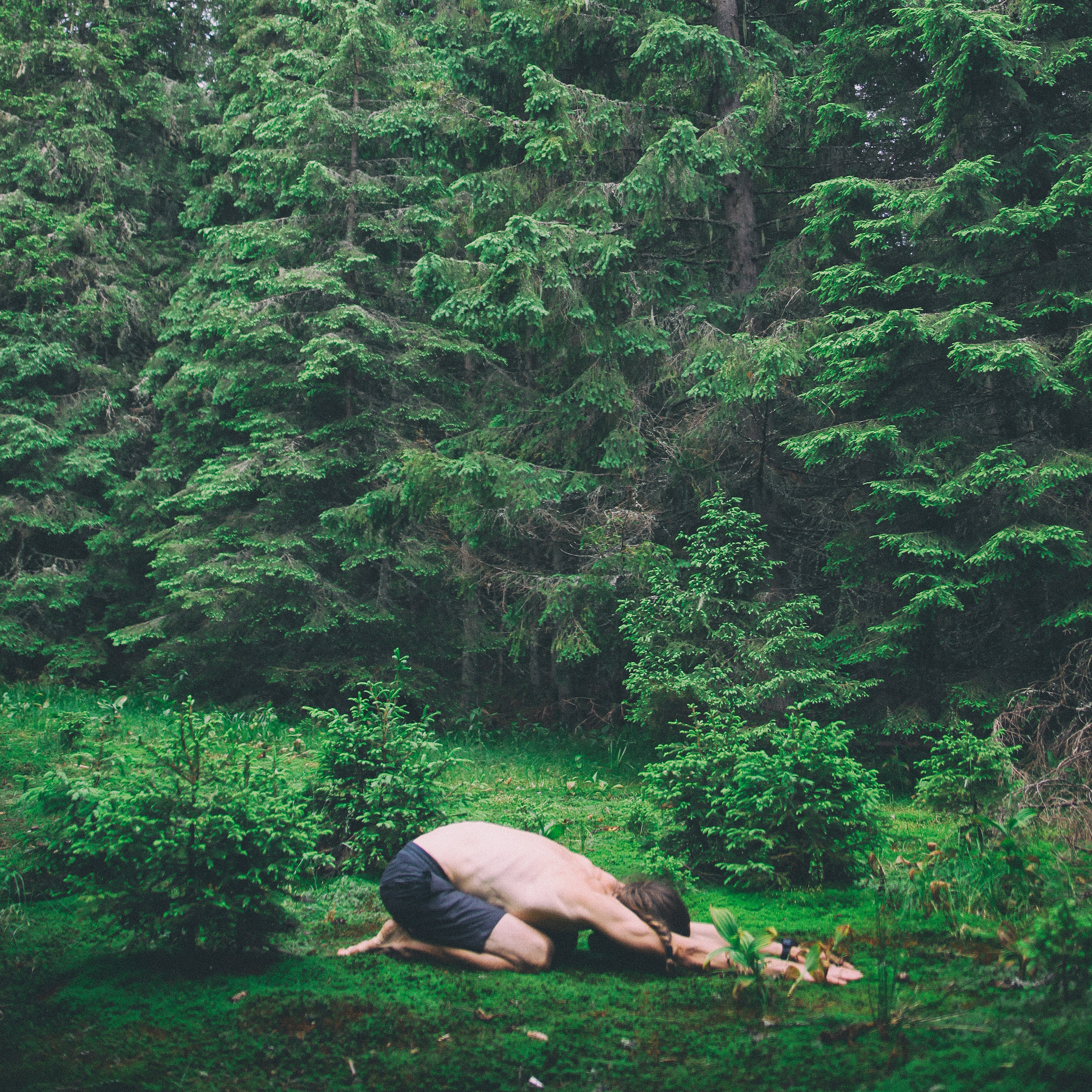A man doing child yoga pose in the forest.
